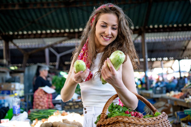 Young caucasian woman buying fresh organic vegetables at market place and holding bag full of healthy food