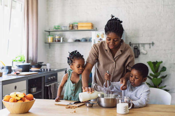 Happy African American mother, daughter and son preparing whipped cream on a wooden kitchen table