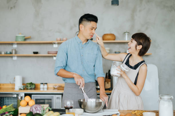 Affectionate young Asian couple having fun and smiling happily while baking together in a domestic kitchen