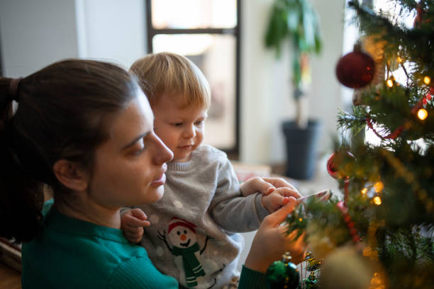 A woman and her baby boy decorating the Christmas tree for a sustainable holiday.