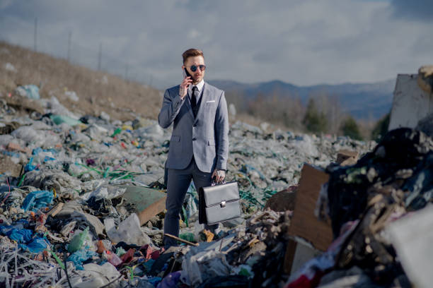 Fashionable modern businessman with smartphone on landfill, consumerism versus pollution concept. Circular economy.