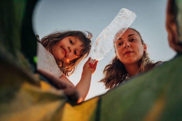View from below of a mother and daughter throwing a plastic bottle on a recycle bin. Zero-waste mindset.