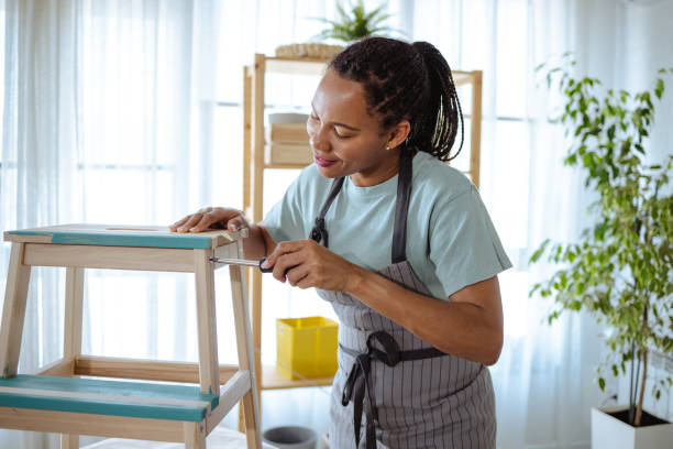 African American mid adult woman preparing wooden chair for painting at home.