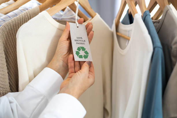 Zero-Waste Fashion Concept. Female hands hold a label from white knitted clothing, on which it says 100% recycle fabric and a recycling sign.