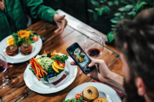 Young couple photographing delicious vegetarian burger and mixed organic salad on white plate in vegetarian restaurant near me.
