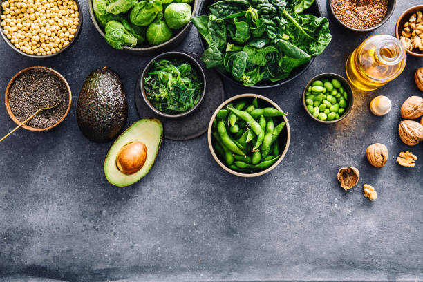 Variety of Omega 3 vegan food items on black table. Table top view of fresh spinach, flax seeds, walnuts, walnut oil bottle, brussel sprouts, lentil seeds, chia seeds, avocado, edamame and wakame in bowls on a table.