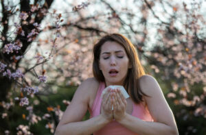 Vegan Diet for Allergies. Pretty young woman sneezing in front of blooming tree.