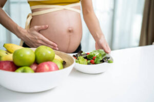 Best vegan foods for pregnancy. Pregnant lady standing beside a white table with some vegan meals.