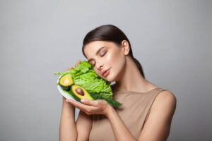 Vegan Diet and Skin Health. Healthy young brunette woman holding healthy eating avocado with green salad.