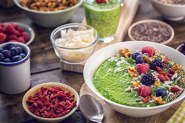 Green breakfast smoothie in bowl with vegan superfoods like chia, quinoa, goji, fresh berries and sunflower seeds.